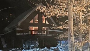 Un edificio de dos plantas con balcón, rodeado de árboles desnudos y nieve.