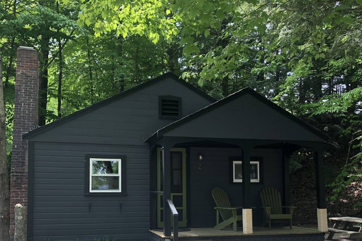 A small cabin with a porch, two Adirondack chairs, and a brick chimney.