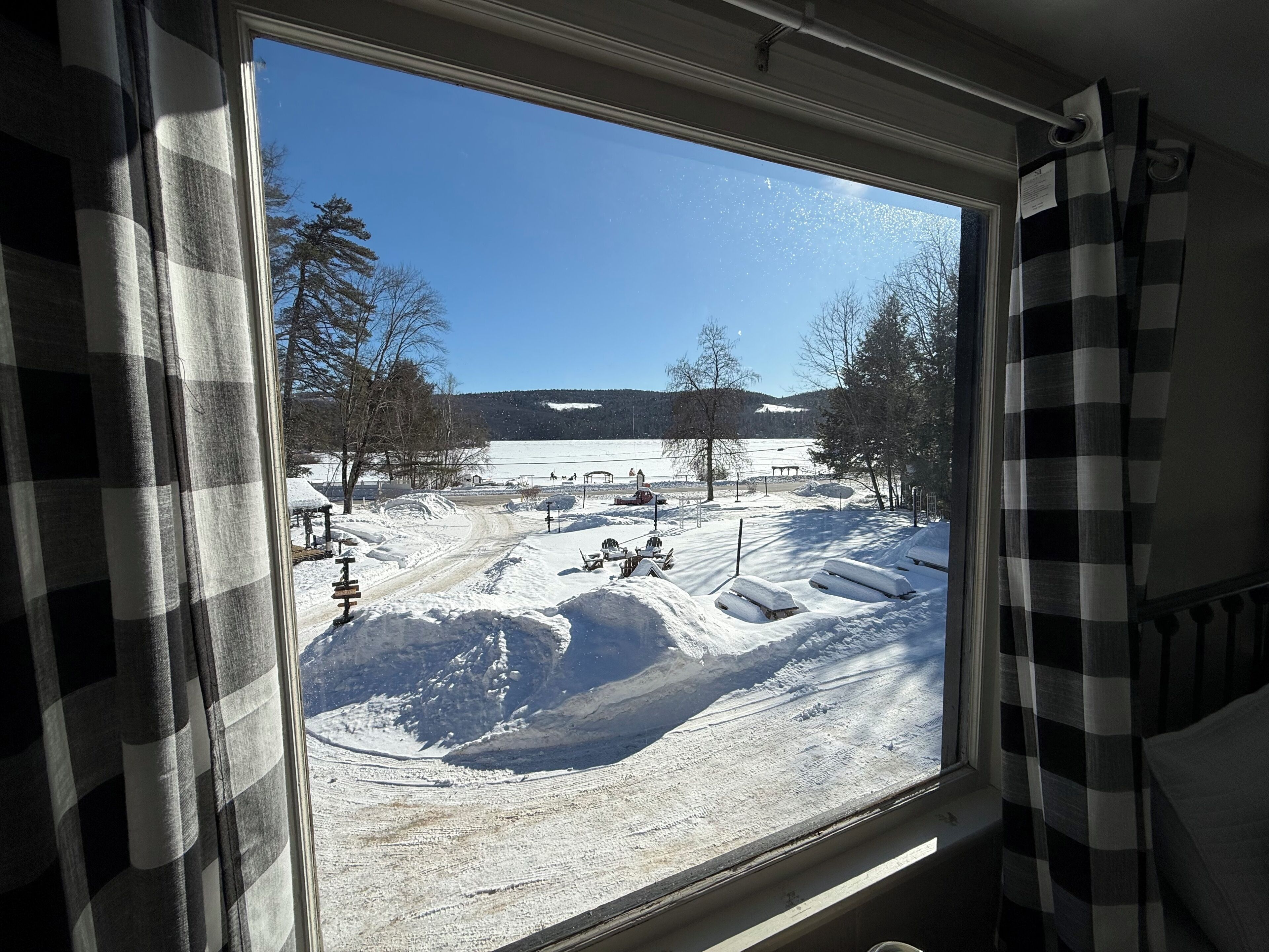 A window with a view of a snowy landscape, including a path, benches, and trees.