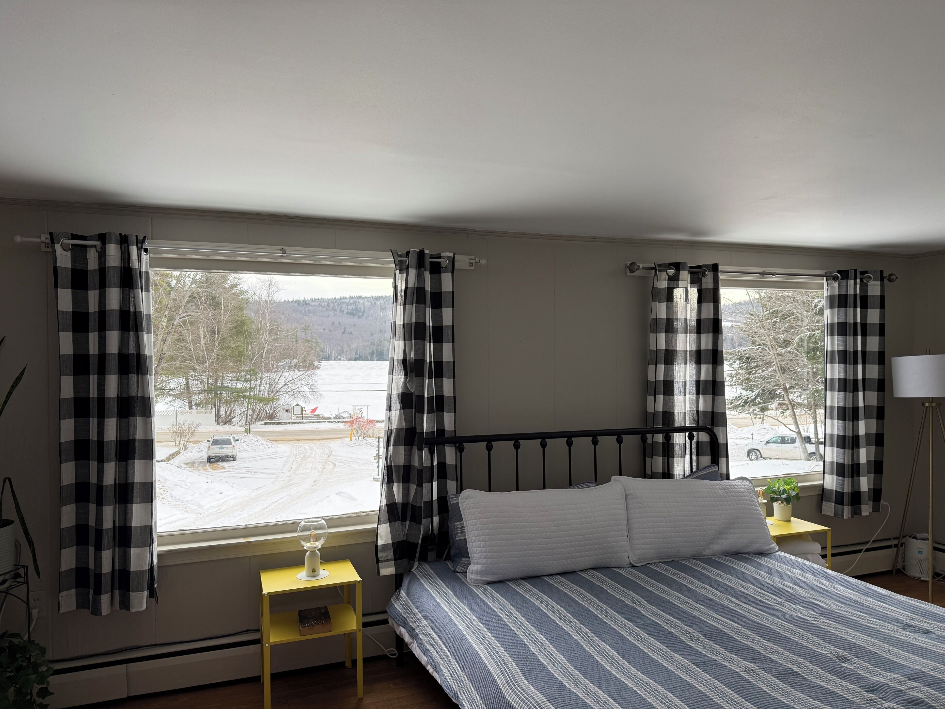 Une chambre à coucher avec un lit, une table de chevet, une lampe et une vue sur un paysage enneigé par la fenêtre.