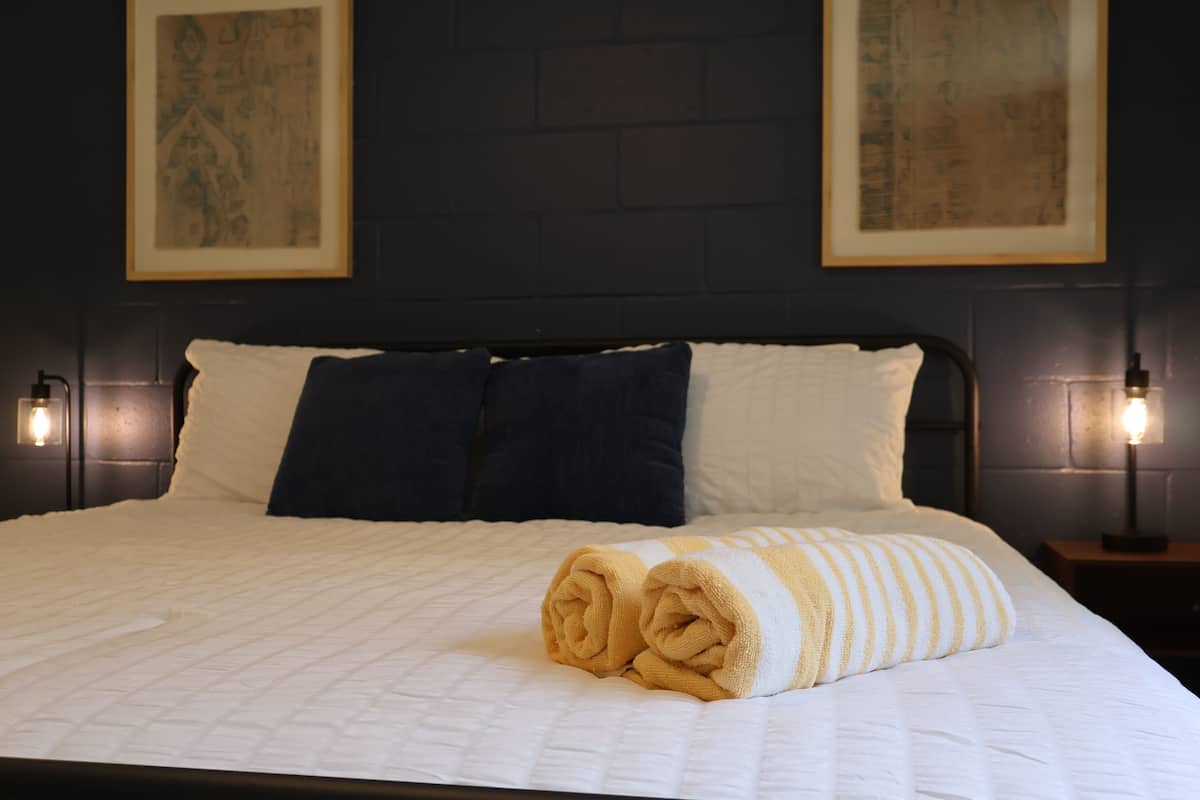 A neatly made bed with white bedding and rolled towels, two pillows, and framed artwork on the wall.