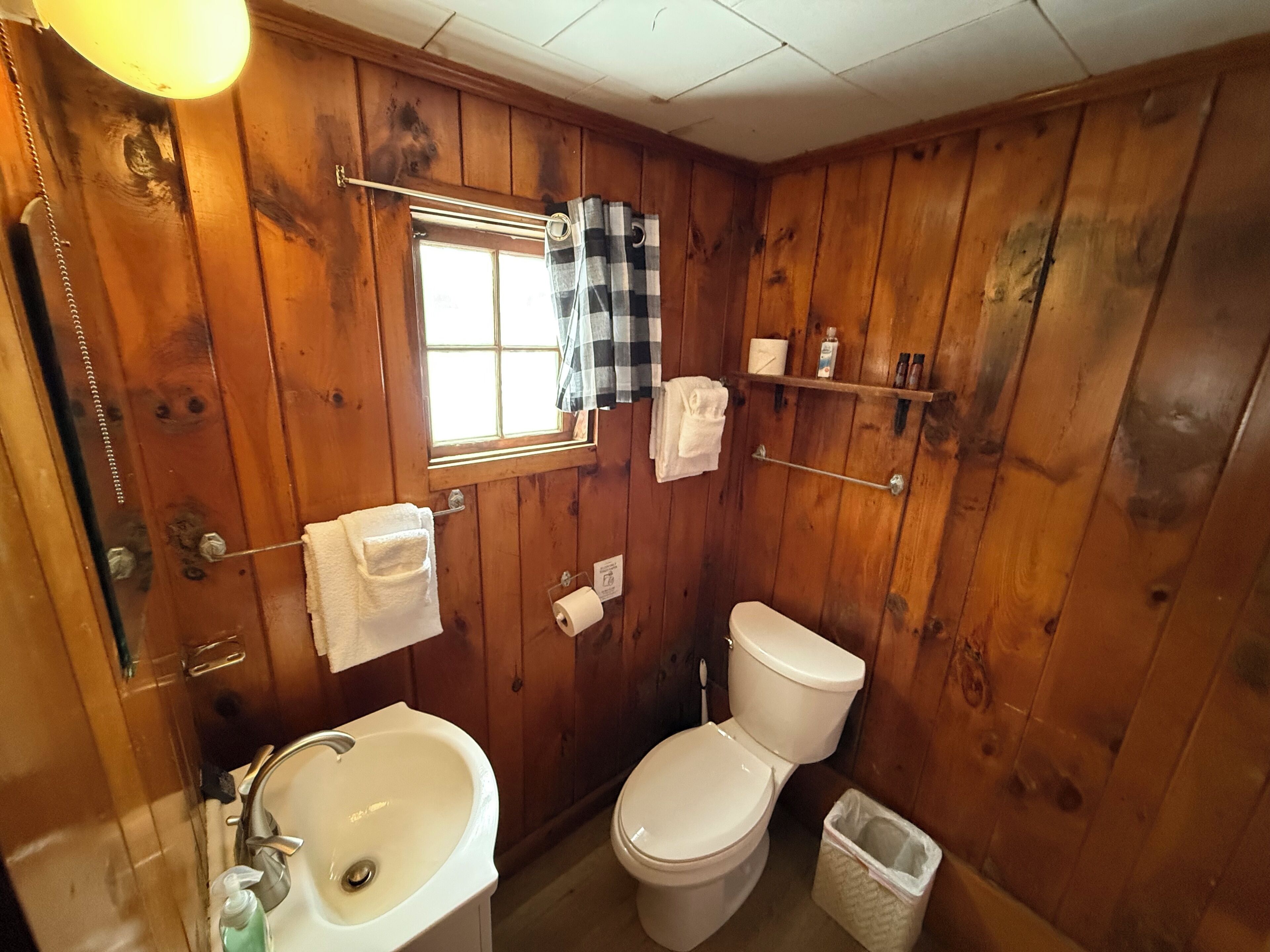 Un baño con paneles de madera, un lavabo, un inodoro y una ventana.