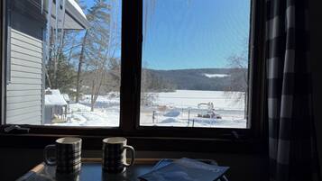 A window with icicles, a view of a snowy landscape, and a table with a mug and a magazine.