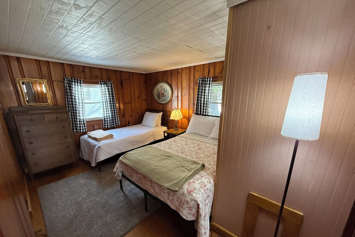 A room with two beds, a dresser, a lamp, and a wall-mounted clock.