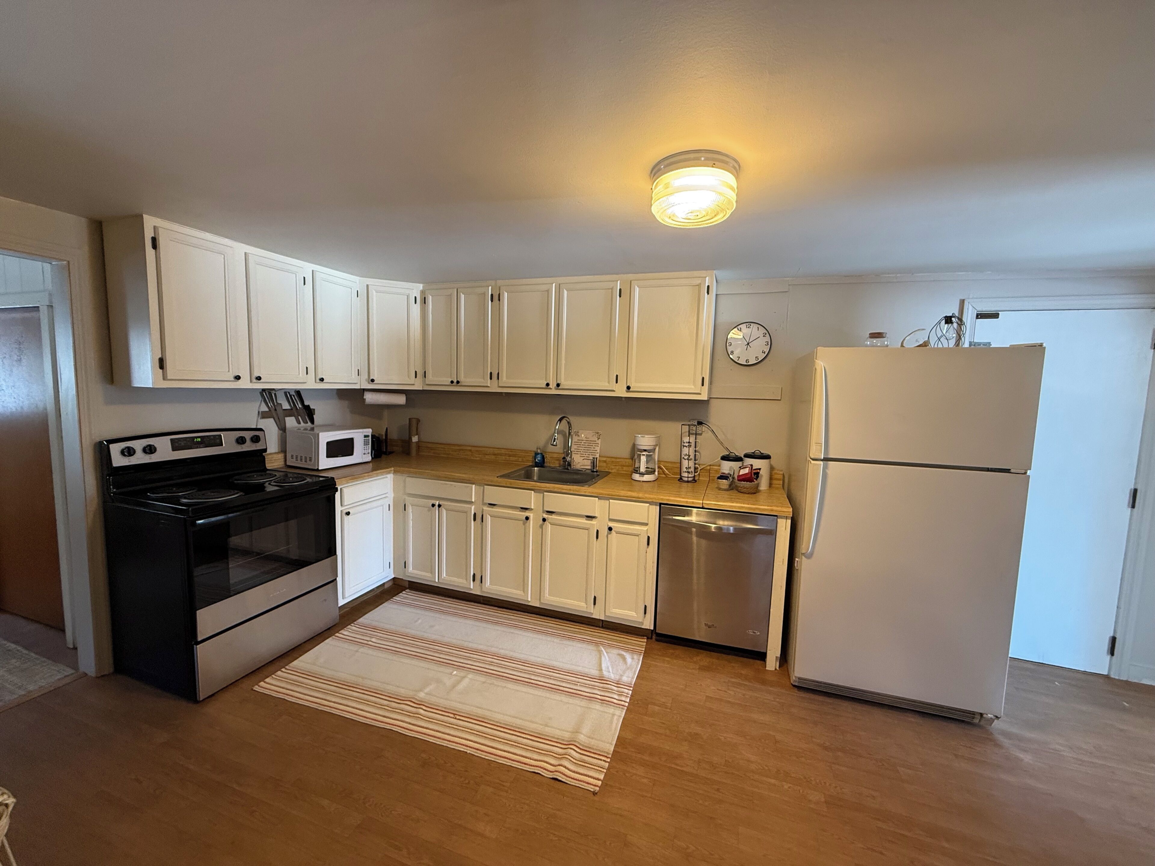A kitchen with white cabinets, a stove, microwave, dishwasher, and a refrigerator.