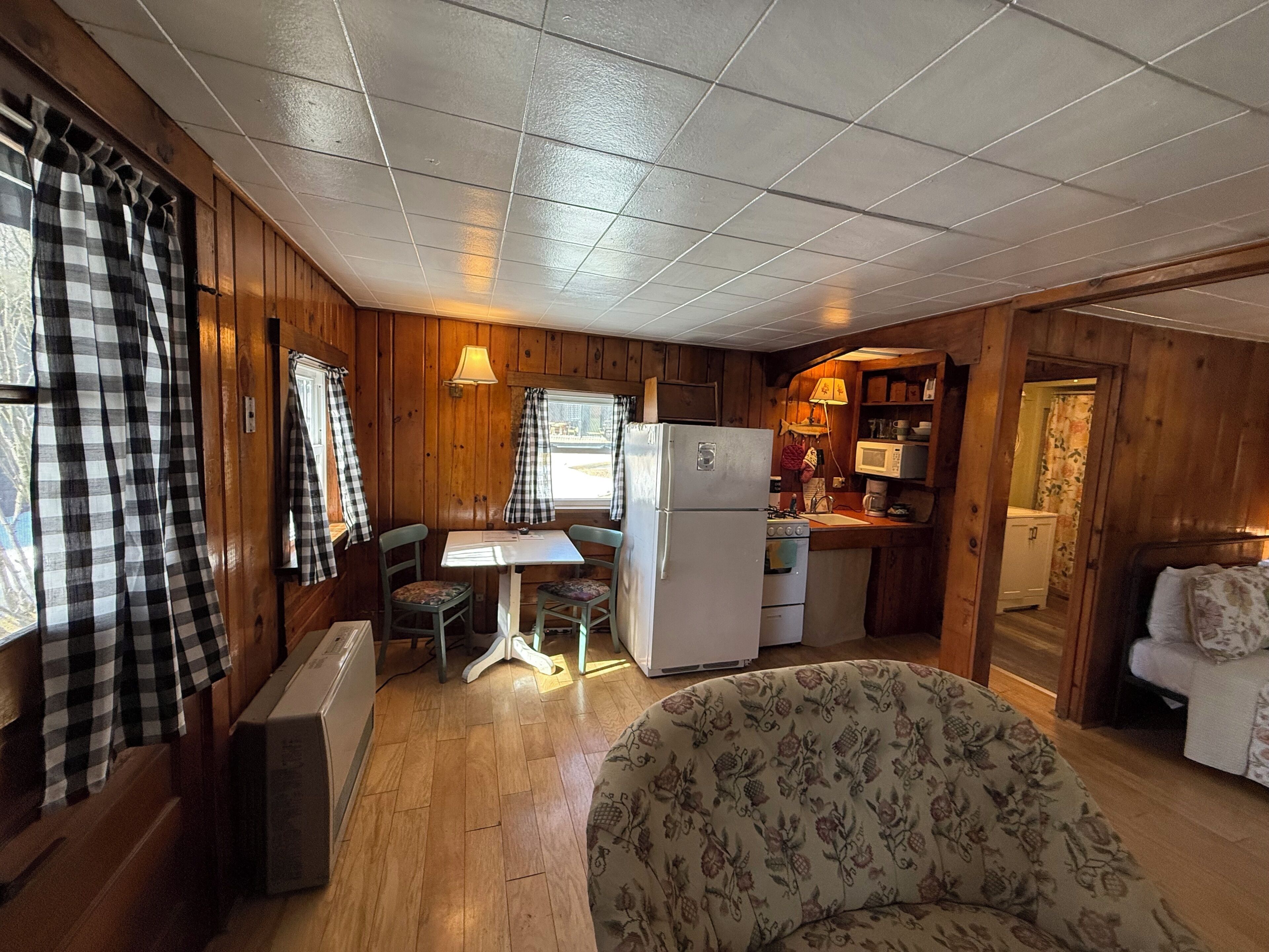 A cabin interior with a dining table, chairs, a refrigerator, a microwave, and a patterned armchair.