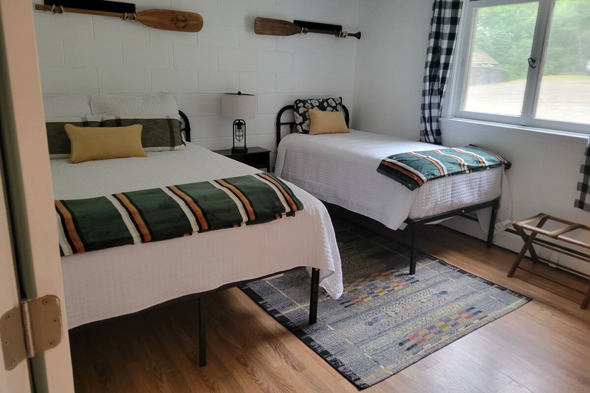 A room with two beds, a window with checkered curtains, and a wooden floor.