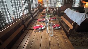 A wooden dining table set with red napkins, plates, and cutlery, flanked by checkered curtains and wooden benches.