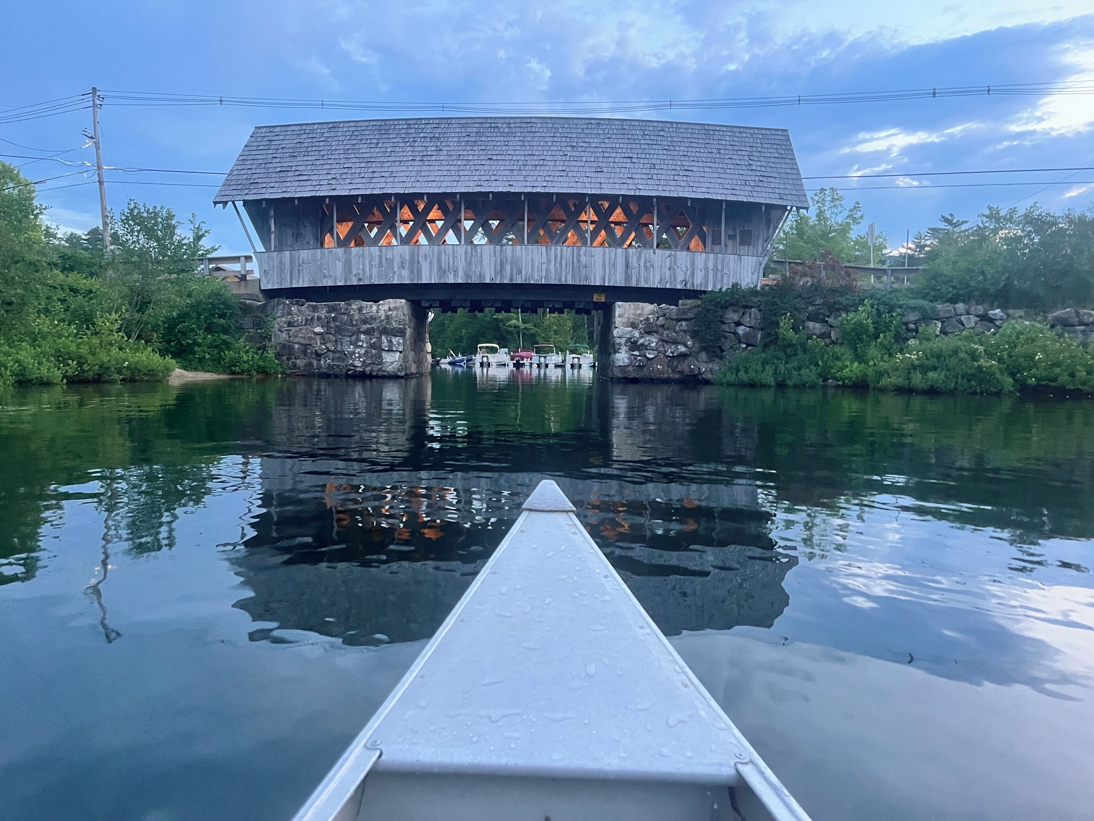 A wooden covered bridge over a calm river with a boat in the foreground.