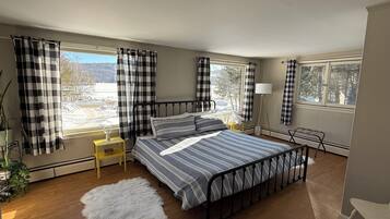 A bedroom with a metal bed frame, a fluffy rug, a bedside table with a lamp, and a view of a snowy landscape through large windows.