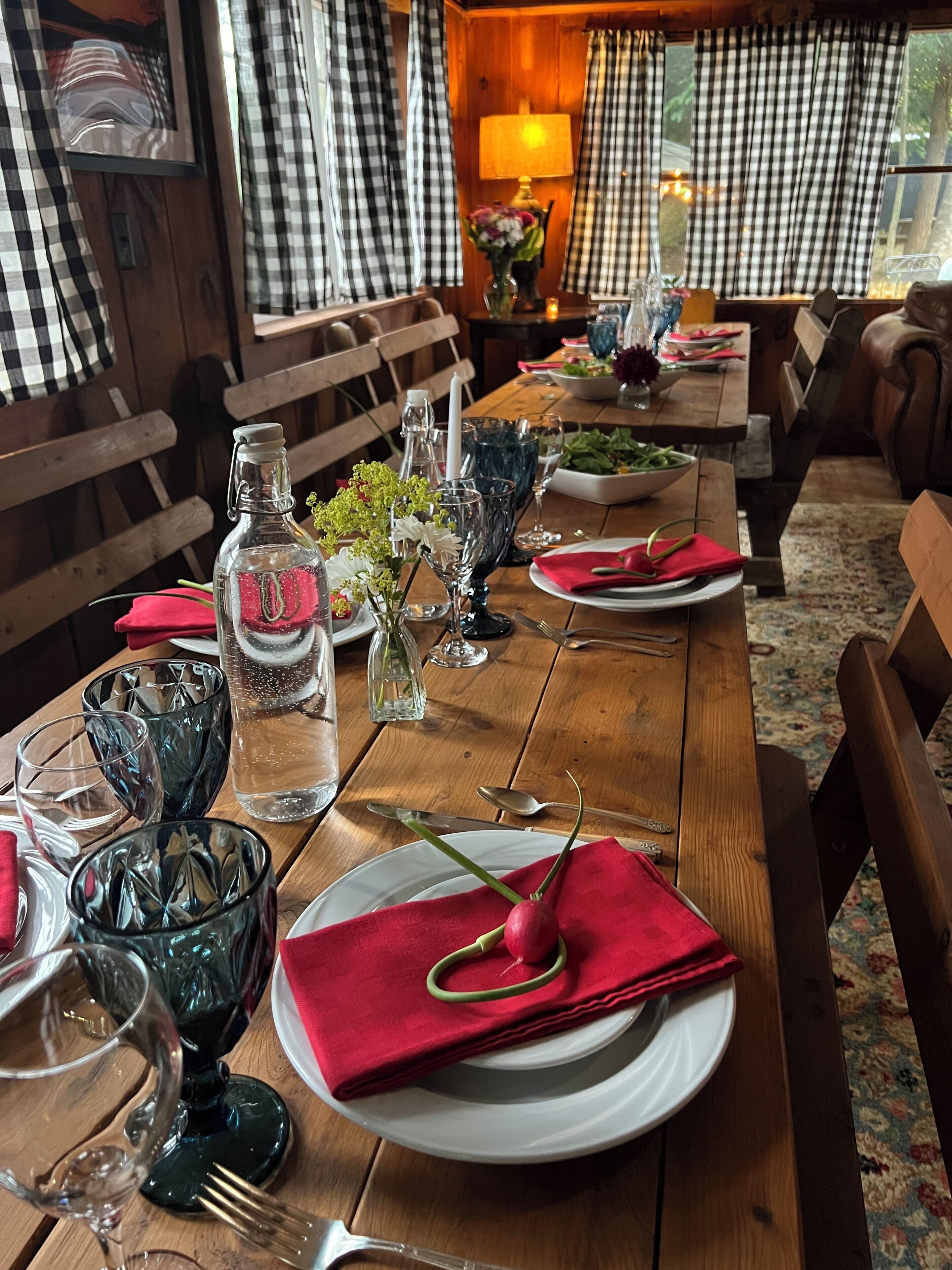 A dining table set with plates, glasses, and cutlery, with a bottle and flowers on the table.