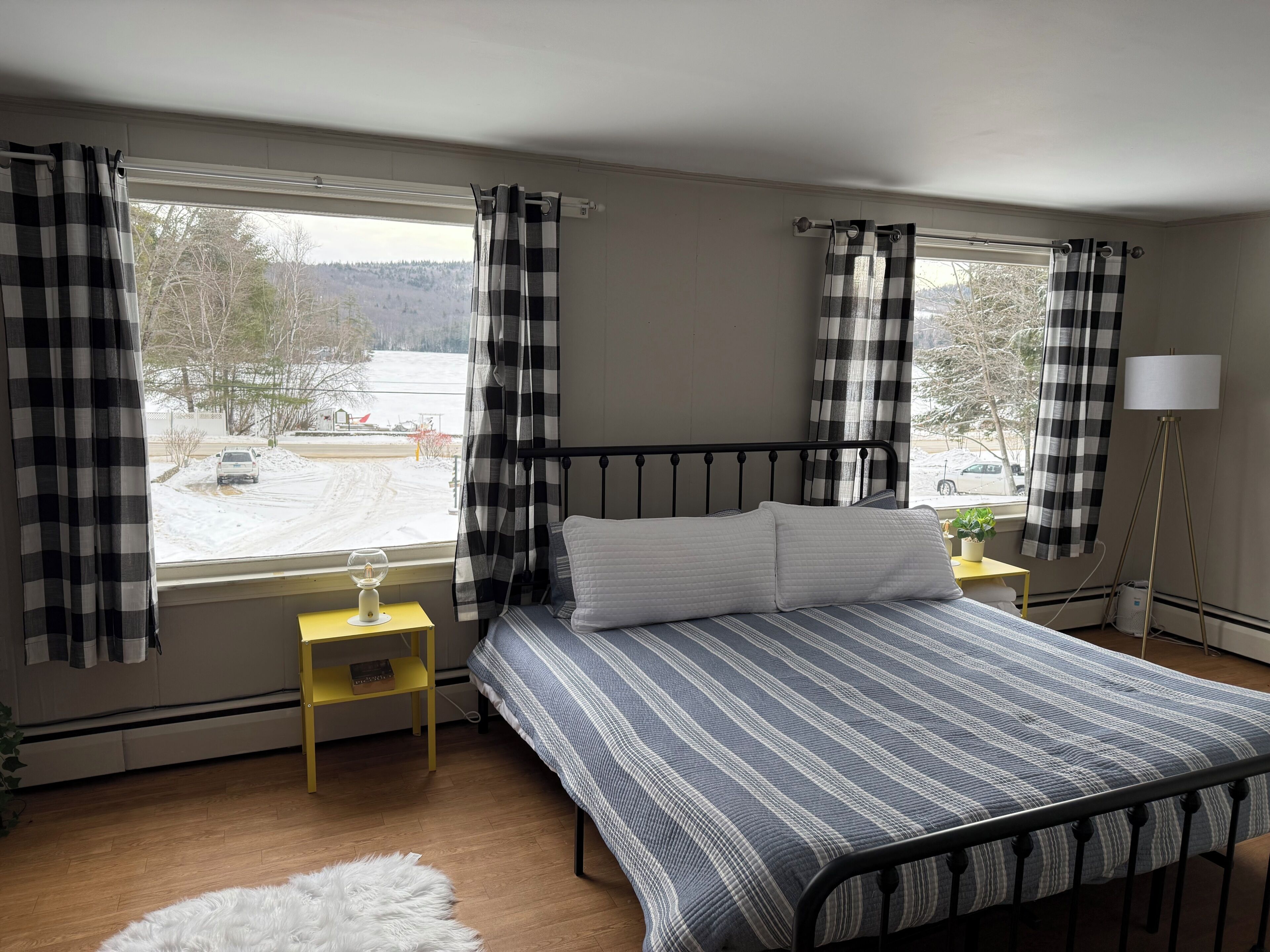 A bedroom with a bed, a nightstand, a lamp, and a view of a snowy landscape.