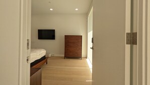 A narrow hallway with a bed, a wooden wardrobe, and a flat-screen TV mounted on the wall.