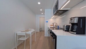 A modern kitchen with white cabinetry, a black refrigerator, a coffee machine, and a dining area with a white table and chairs.