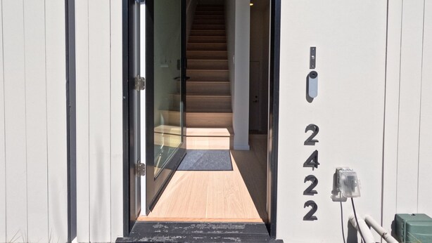 A modern building entrance with a glass door, a wooden staircase, and a number plaque.