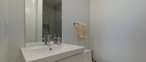 Une salle de bain moderne avec un lavabo blanc, des toilettes et un miroir au-dessus du lavabo.