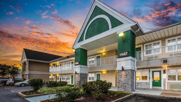 Un motel à la façade verte et blanche, portant le numéro 11457, avec une structure à deux étages et un balcon au niveau supérieur.