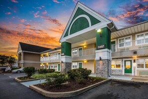 Un motel à la façade verte et blanche, portant le numéro 11457, avec une structure à deux étages et un balcon au niveau supérieur.