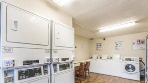 Une buanderie équipée de machines à laver et de sèche-linge superposés, avec un plancher en bois et une table entourée de chaises.