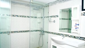 A modern bathroom with a glass-enclosed shower, white tiled walls, and a white sink with a mirror above it. - Hotel pool city  (Bonao)