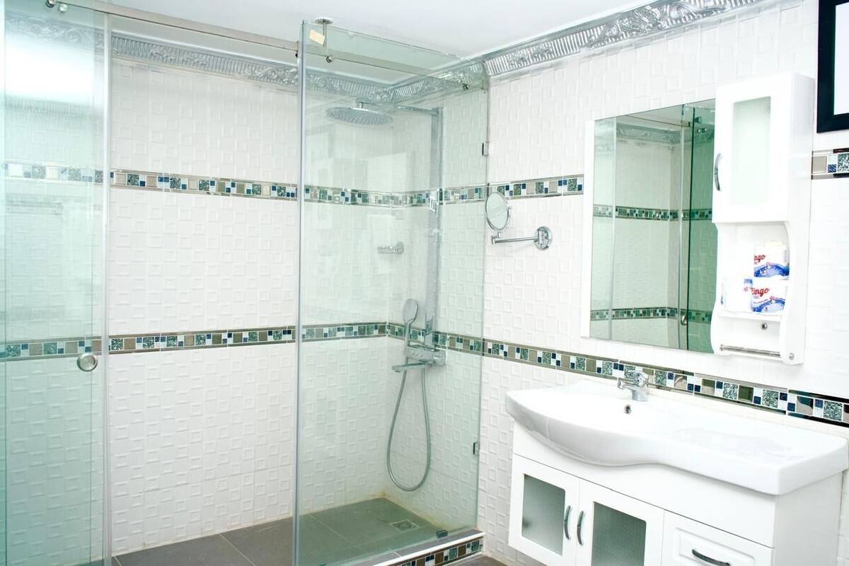 Un baño moderno con ducha cubierta por vidrio, paredes de azulejos blancos y un lavamanos blanco con un espejo encima.