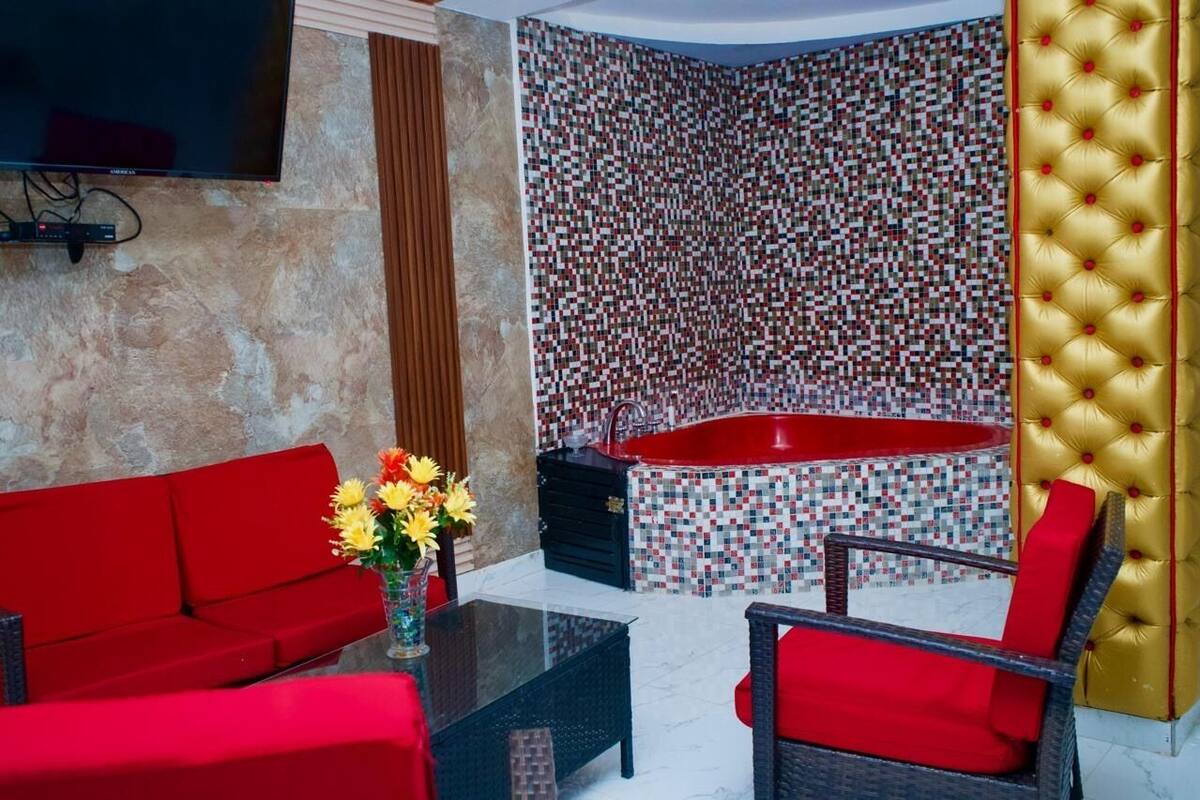 Un baño moderno con pared de mosaicos, una bañera roja y un panel de pared tapizado en dorado.