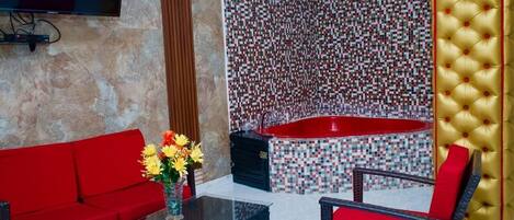 A modern bathroom with a mosaic wall, a red bathtub, and a gold tufted wall panel.