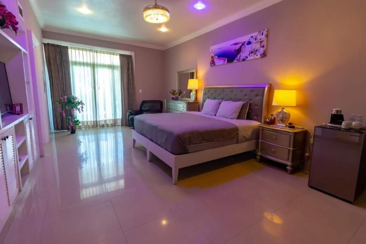 Une chambre d’hôtel avec un grand lit, des tables de chevet, un bureau, une chaise, une télévision, une armoire et une fenêtre avec des rideaux.