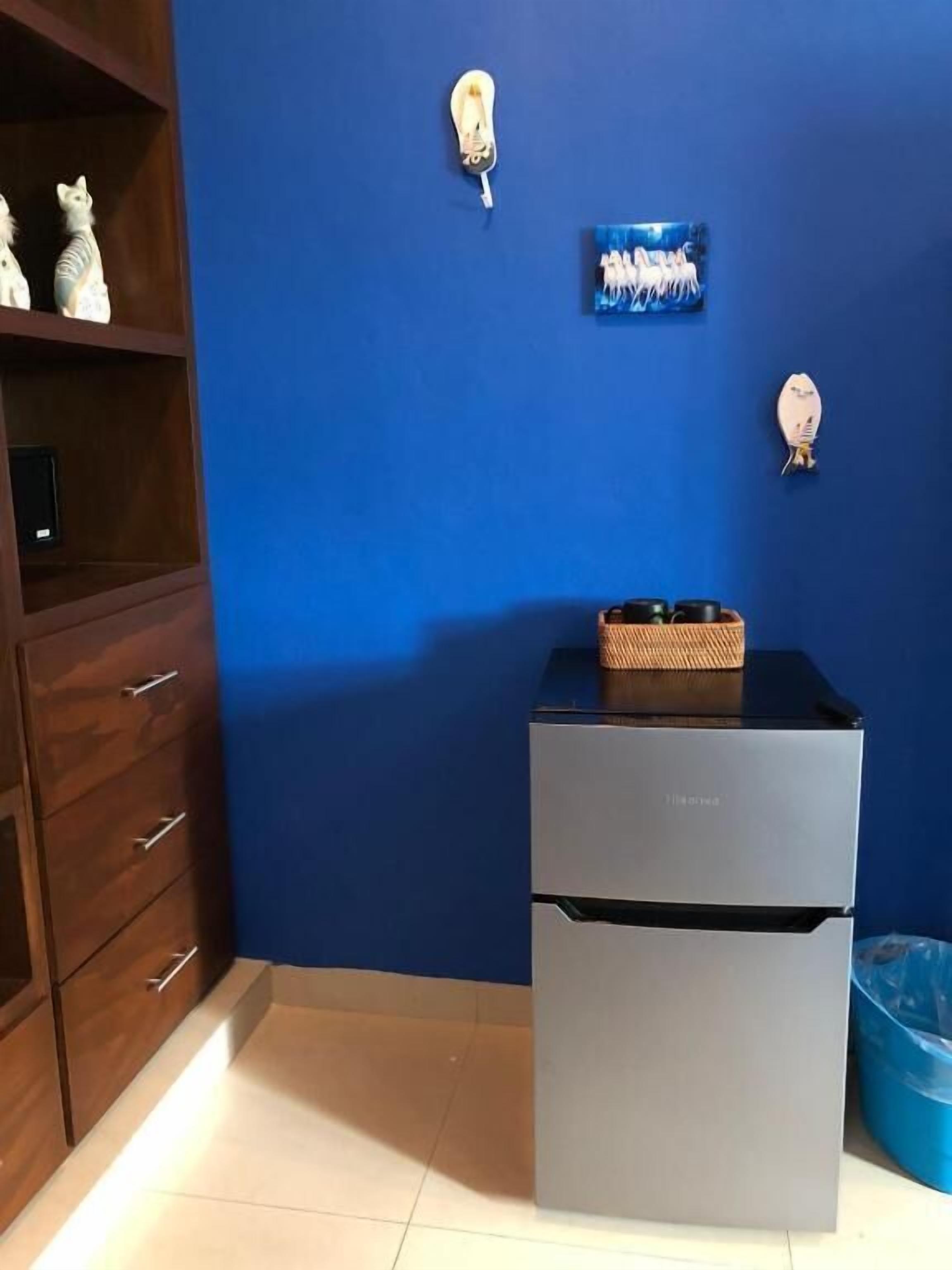 Una kitchenette compacta con refrigerador integrado, un armario de madera y una pared azul decorada.