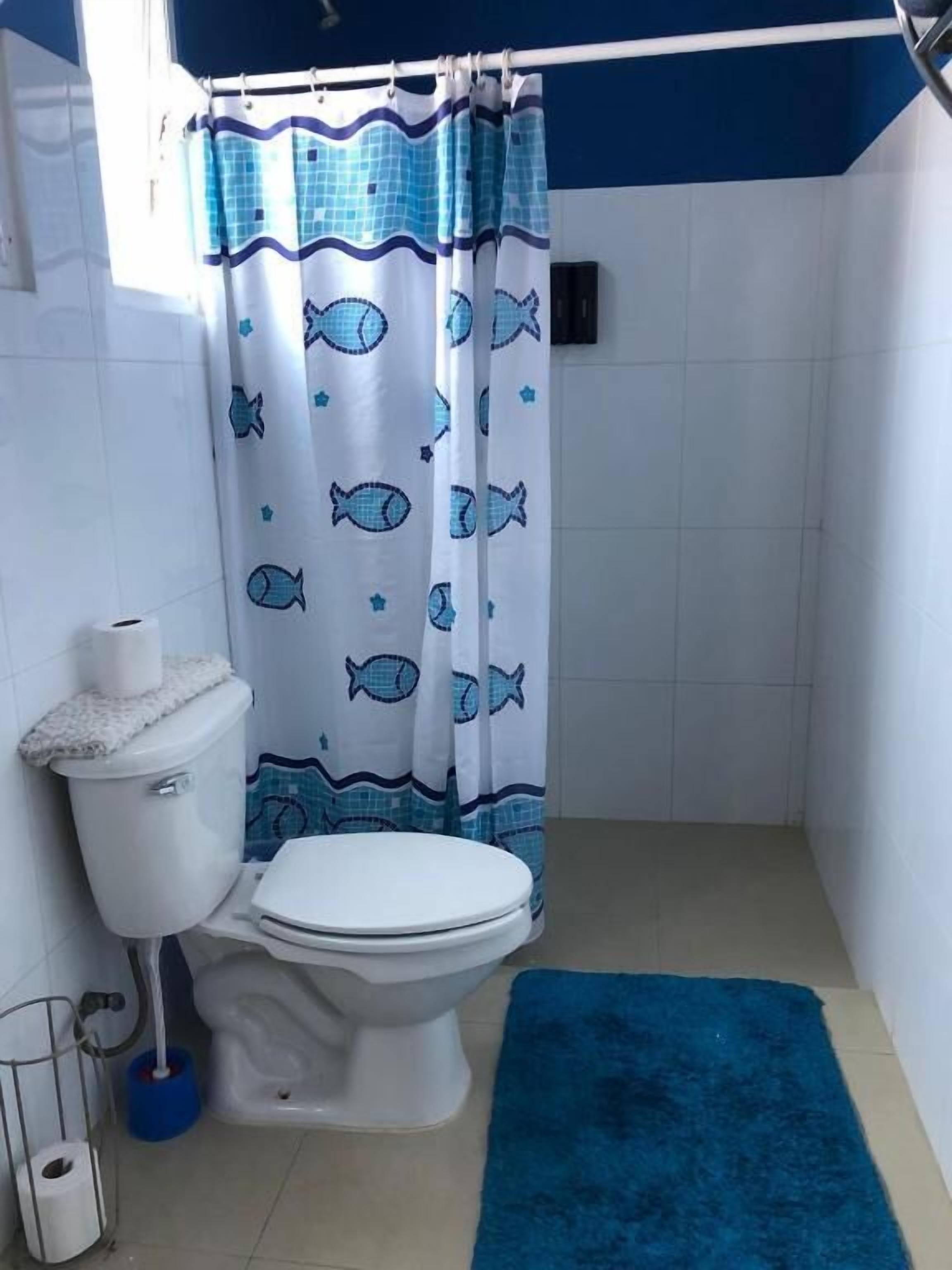 A bathroom with a toilet, a blue shower curtain with fish patterns, and a blue bath mat.