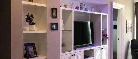 Una sala de estar con televisor de pantalla plana, estanterías empotradas y un tapete decorativo.