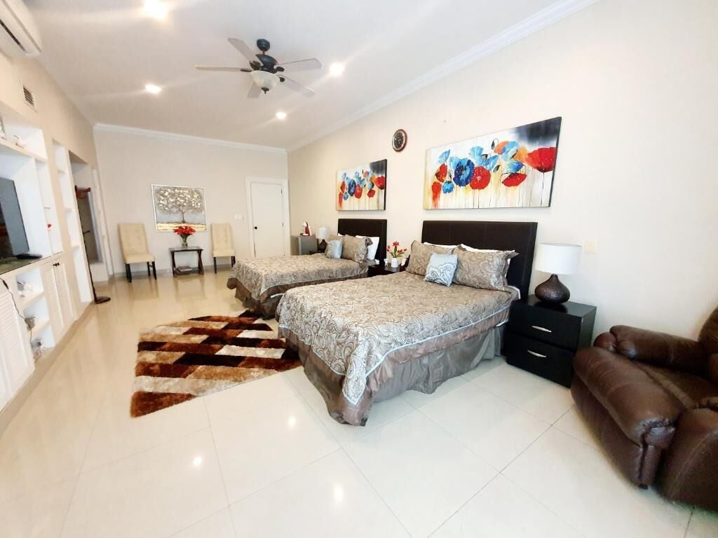 A bedroom with two beds, a ceiling fan, artwork on the walls, and a brown leather chair.