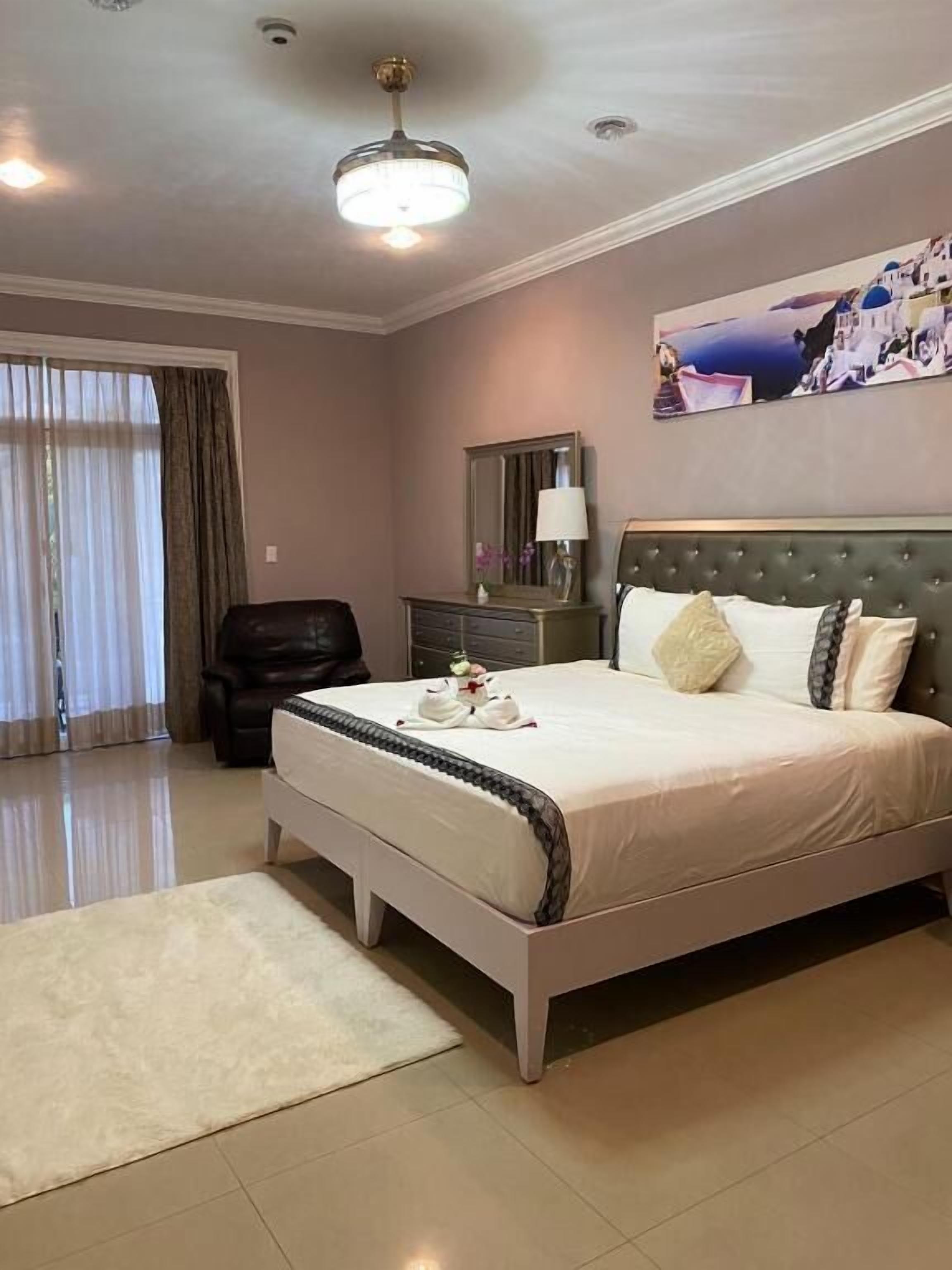 Une chambre d’hôtel avec un lit, une chaise, une commode, un miroir et un ventilateur de plafond.