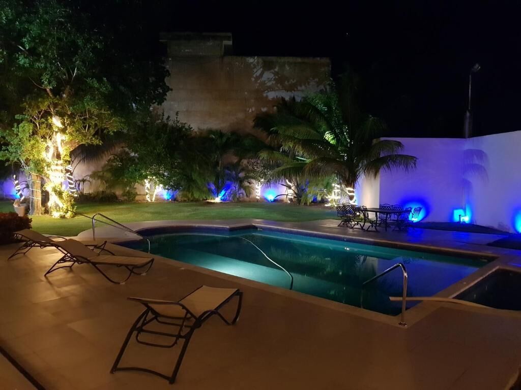 Uma área de piscina à noite com espreguiçadeiras, piscina e iluminação ambiente.