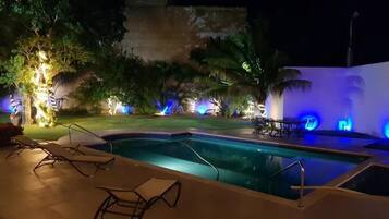 Uma área de piscina à noite com espreguiçadeiras, piscina e iluminação ambiente.