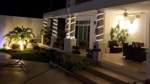 Un edificio de dos pisos con balcón, zona de estar exterior y columnas iluminadas.