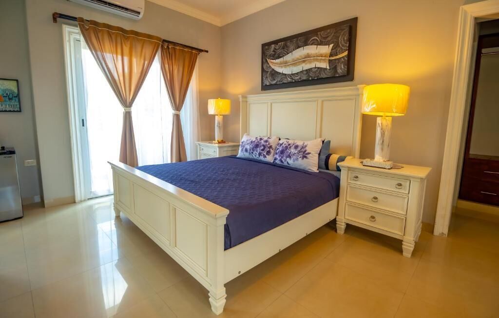 A bedroom with a bed, nightstands, a lamp, a painting, and a door.