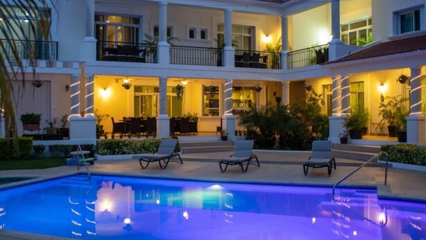 Un hotel de varios pisos con piscina, mobiliario exterior y balcones bien iluminados.