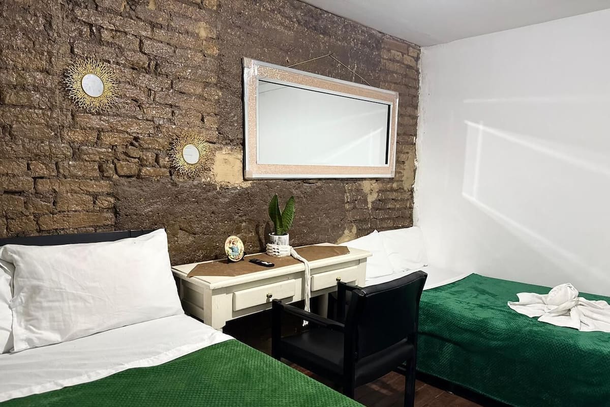 Ein Hotelzimmer mit Backsteinwand, einem Bett, einem Schreibtisch mit Stuhl, einer kleinen Topfpflanze und einem Spiegel.