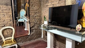 A room with a stone wall, a television, a glass table, a chair, and a mirror. - Casa Cordoba (Bogotá)
