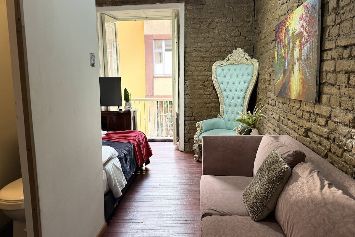 Ein Zimmer mit Bett, Sofa, Fernseher, Balkon und einer Ziegelwand.