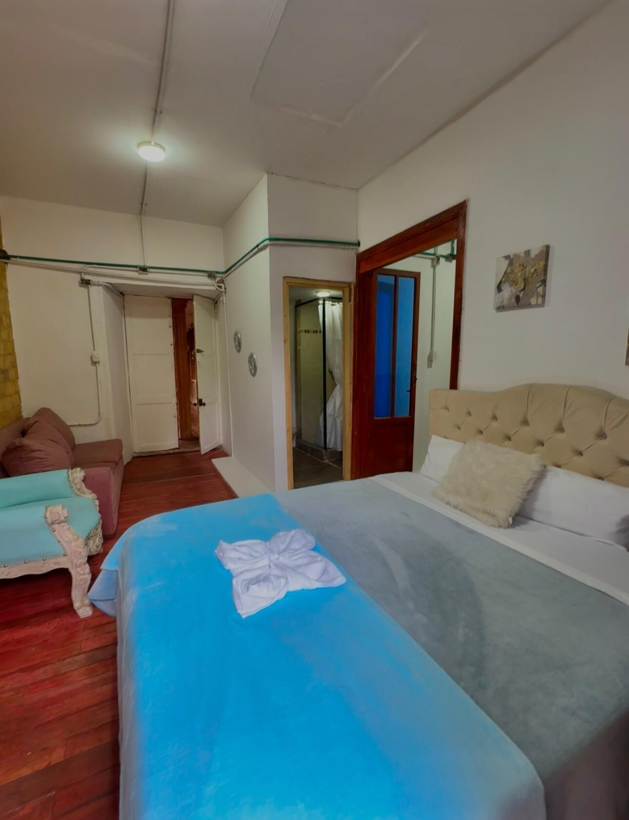 A hotel room with a bed, a sofa, a mirror, and a door leading to a bathroom.