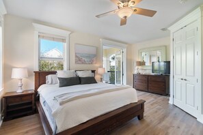 Ein Schlafzimmer mit Bett, Deckenventilator, Kommode, Fernseher und einer Tür.