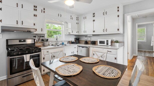 A modern kitchen with white cabinets, stainless steel appliances, and a dark wooden dining table with woven placemats.