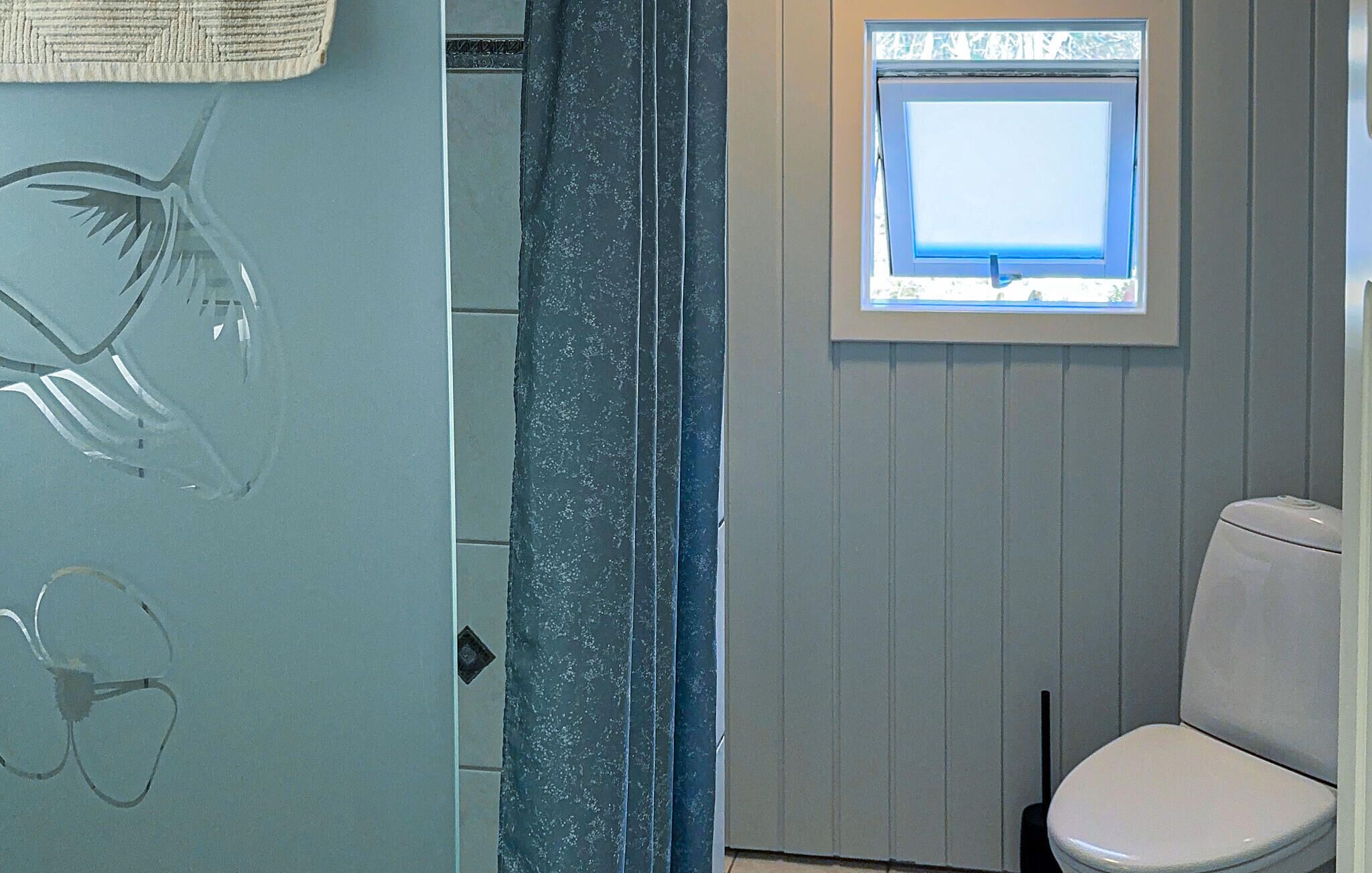 A bathroom with a toilet, a small window, and a shower area.