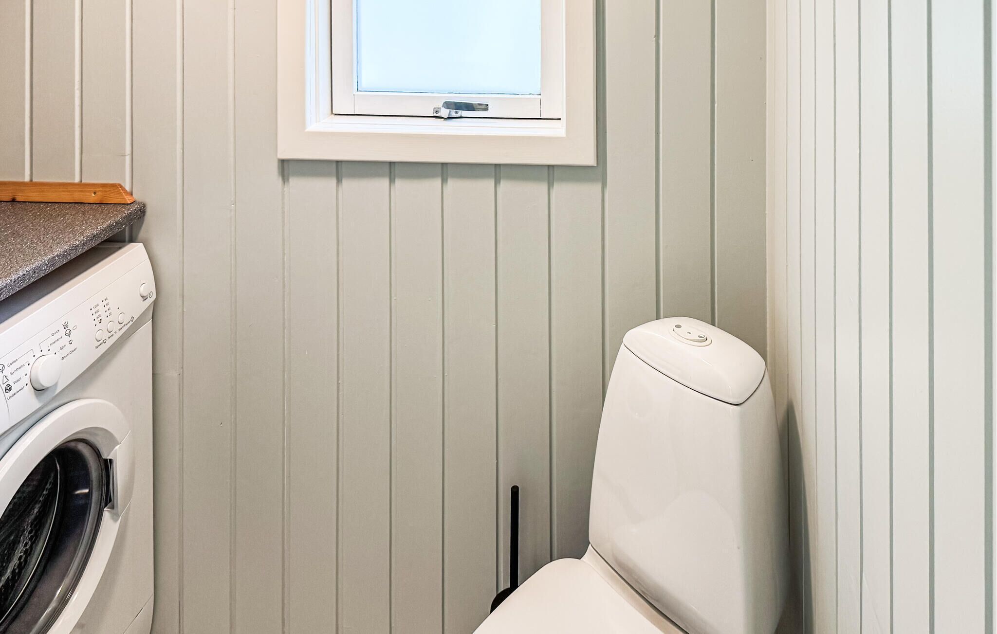 A compact bathroom with a washing machine, a toilet, and a window.