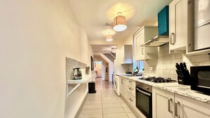 A narrow kitchen with white cabinets, a stove, and a microwave. - Spacious, Cosy & Modern Home w/ Parking , Wi-Fi and Garden (coventry west midlands)