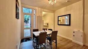 A dining area with a wooden table and chairs, a chandelier, a large mirror, and a view through a window. - Spacious, Cosy & Modern Home w/ Parking , Wi-Fi and Garden (coventry west midlands)