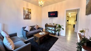 A modern living room with a grey sofa, a wooden coffee table, and a TV displaying 'NETFLIX'. - Spacious, Cosy & Modern Home w/ Parking , Wi-Fi and Garden (coventry west midlands)