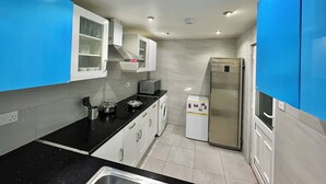 Una cocina moderna con armarios blancos, encimera negra y refrigerador de acero inoxidable.